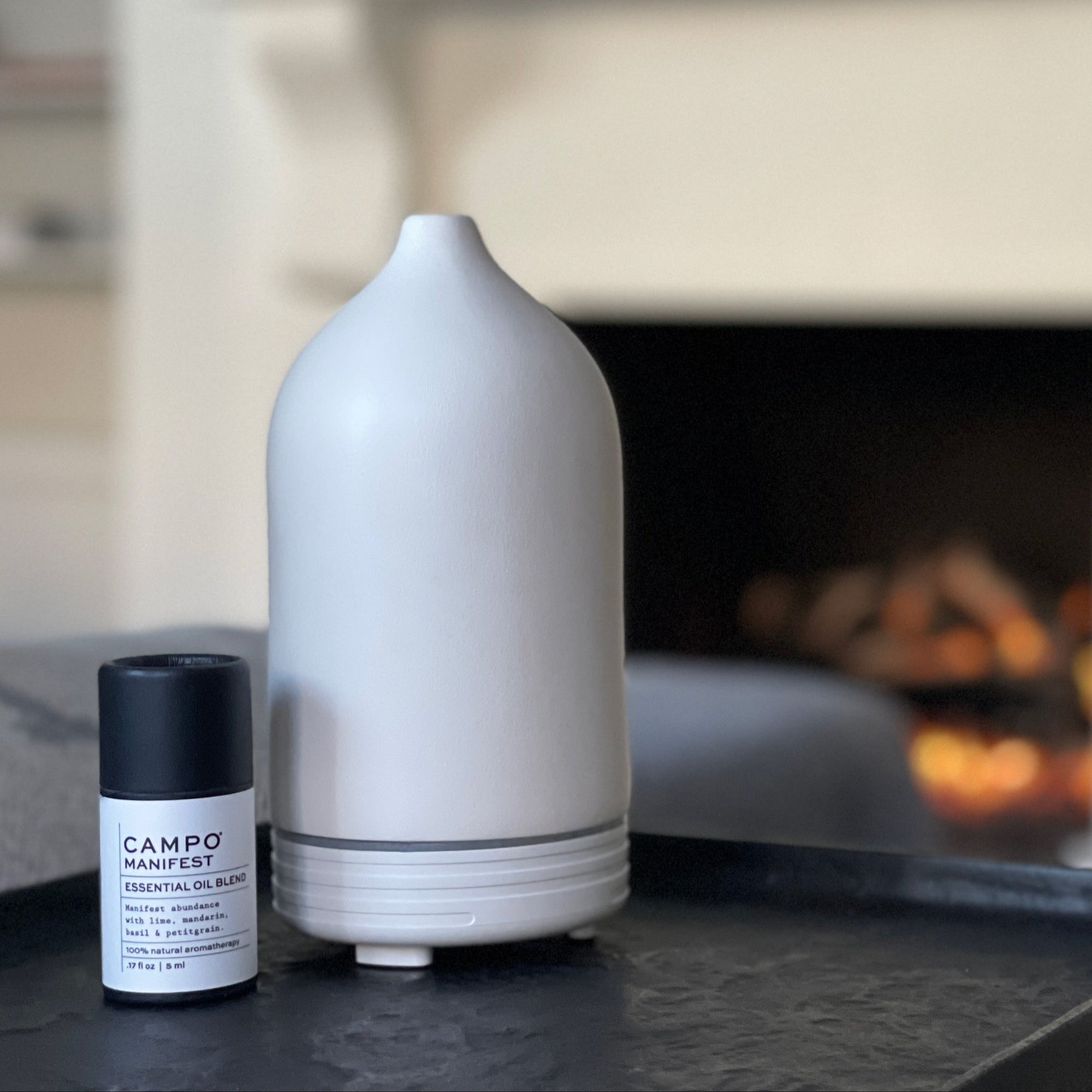 White diffuser and black bottle on a table with a fireplace in the background